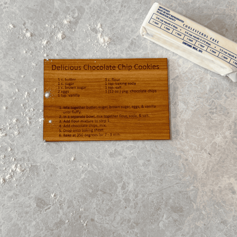 Wooden engraved recipe card on a floured countertop next to a wrapped stick of butter.