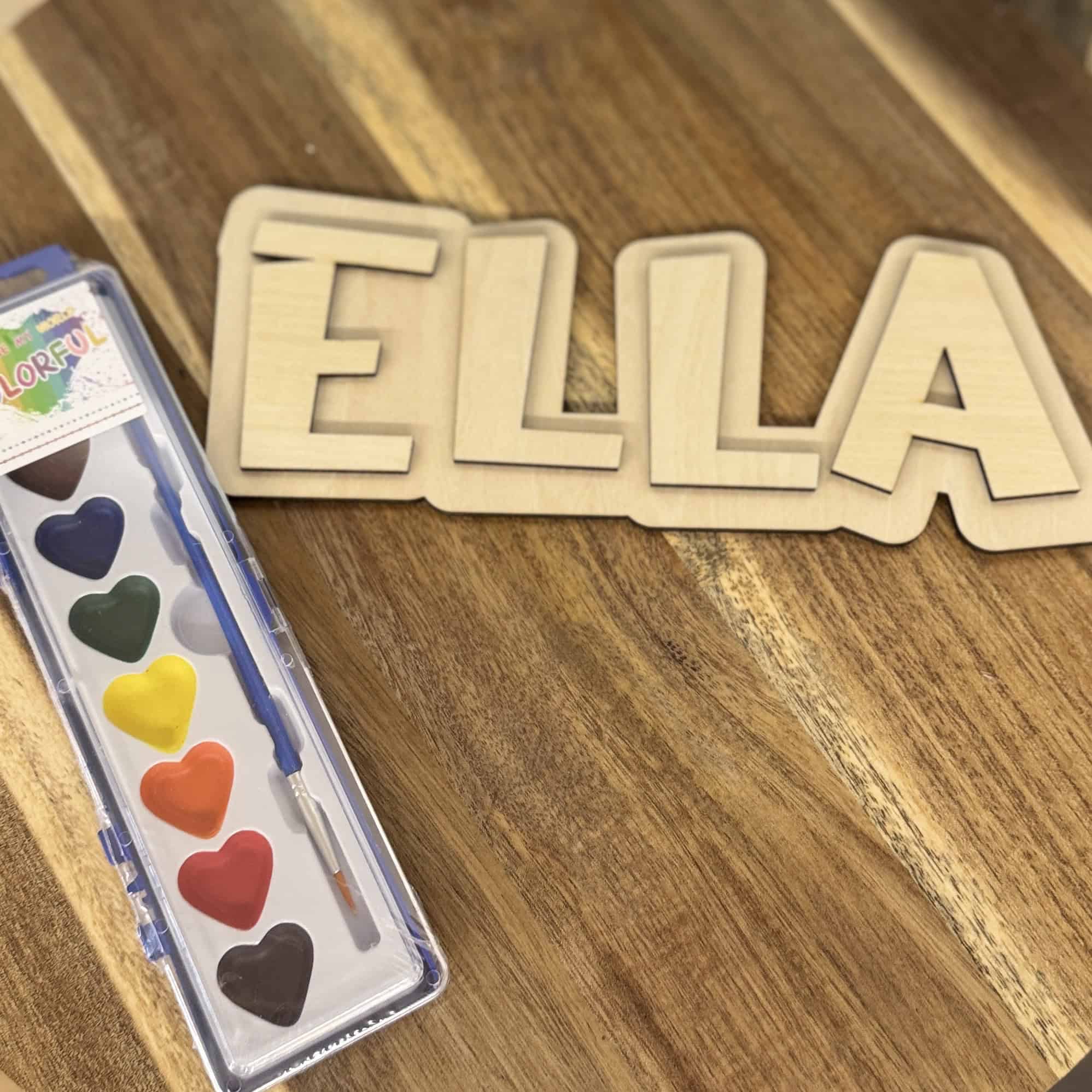Personalized wooden name sign ready to paint with heart-shaped watercolor paints and brush on a wood surface