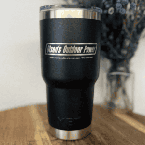 Matte black YETI stainless steel tumbler engraved with a custom business logo in silver laser etching, sitting on a wooden surface.