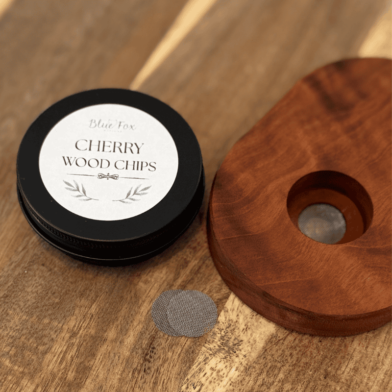 Cherry wood whiskey smoker top with removable screen next to Blue Fox cherry wood chips tin