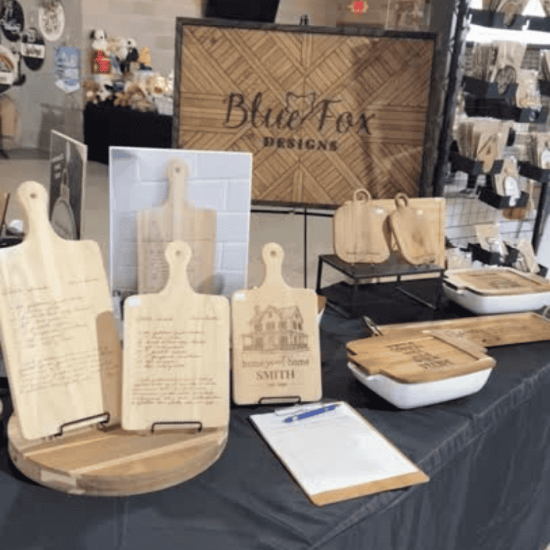 Blue Fox Designs booth display featuring engraved recipe cutting boards made from handwritten family recipes at a craft fair