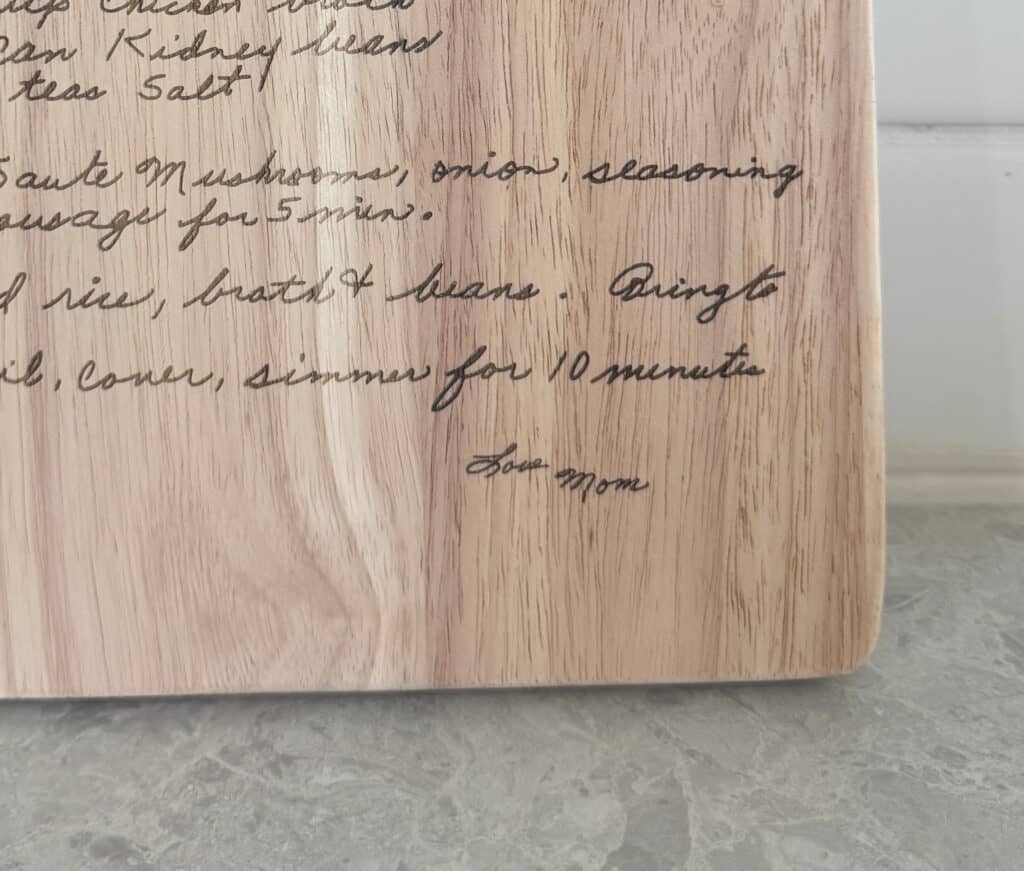 close-up of engraved handwritten family recipe on a wooden cutting board with visible wood grain and “love mom” signature