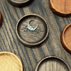 Collection of small wooden ring dishes in different wood tones, including engraved personalized ring holders and plain jewelry trays.