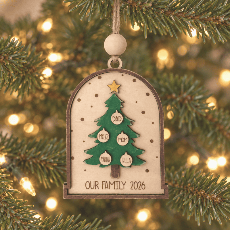 Personalized wooden Christmas ornament hanging on a tree, featuring a green Christmas tree with family names on small ornaments and “Our Family 2026” engraved at the bottom.