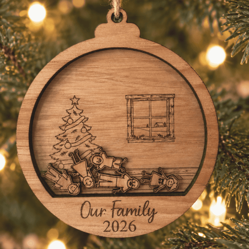 Wooden family ornament hanging on a Christmas tree, featuring little wooden people, an engraved Christmas tree and window, and “Our Family 2026” at the bottom.